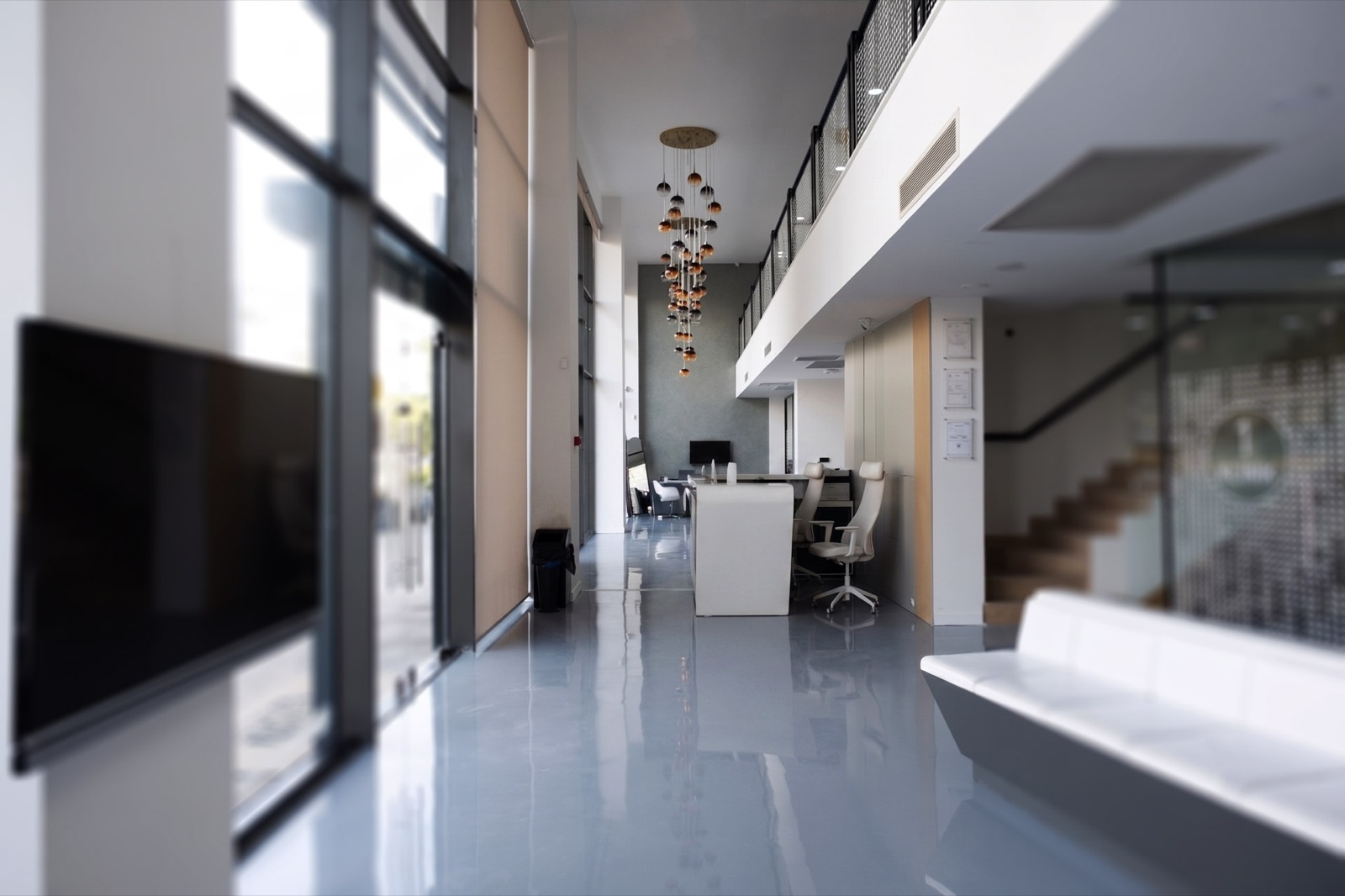 Bright, glass-walled entrance atrium with a hanging chandelier and staircase